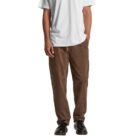 Man wearing a white t-shirt, brown pants, and black shoes, hands in pockets.