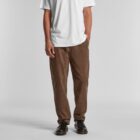 Person wearing a white t-shirt, brown pants, and black shoes standing against a gray background.