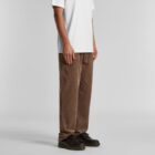 Person wearing a white t-shirt, brown pants, and black shoes standing against a plain background.