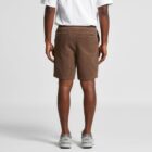 Man in brown shorts, white shirt, and gray sneakers standing facing away from the camera.