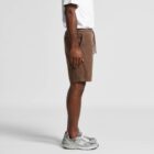 Person in brown shorts, white shirt, and gray sneakers standing in profile against gray background.
