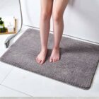 Person standing on a gray bath mat next to a bathtub and a handheld showerhead.