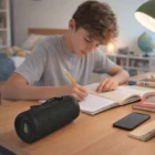 A boy studies at a desk with Black Bluetooth Speakers, his smartphone, and a lamp nearby.