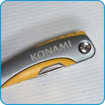 A close-up of a folding knife handle with the word KONAMI engraved on it.