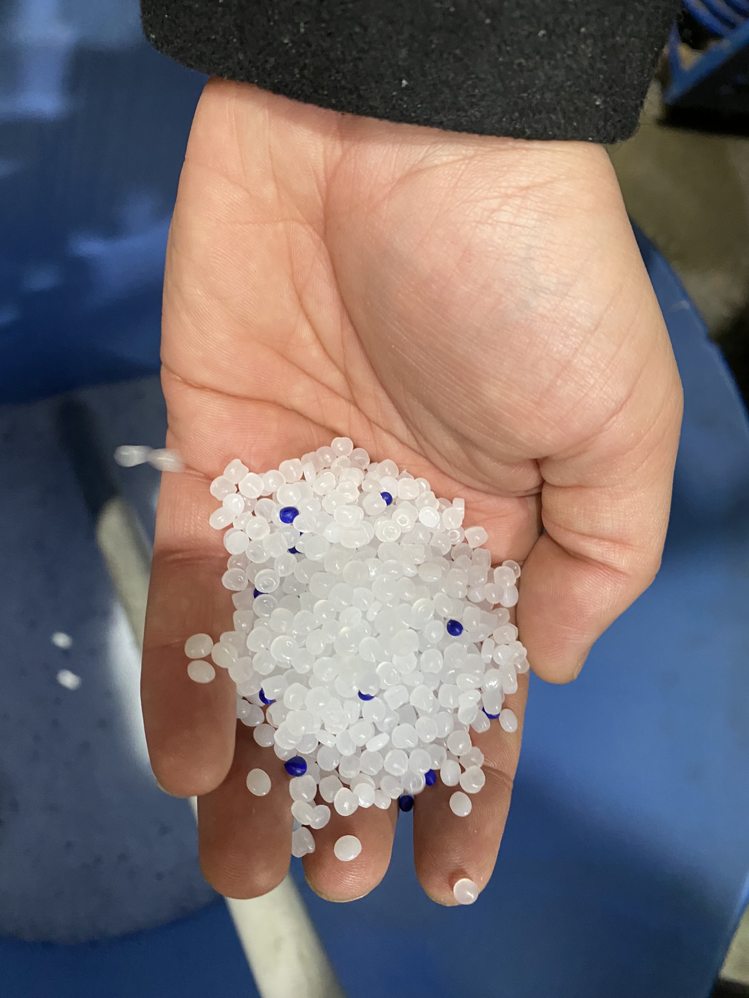 A hand holding plastic pellets, used in custom bottles, above a blue surface.