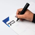 A hand writes Meeting @ 9am on a Magnetic Writing Whiteboard (210mm x 297mm) with a black marker.