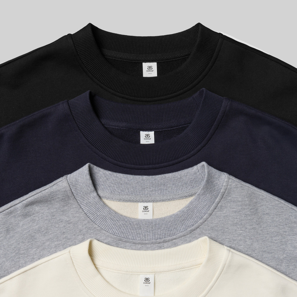 Four AS Colour crewneck sweatshirts stacked in black, navy, gray, and off-white tones.