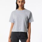 A woman in a grey t-shirt and black jeans stands against a plain white background.