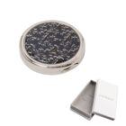 Round silver compact mirror with black floral design, next to an open white Cacharel box.