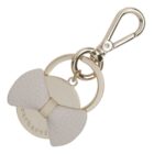 Gold keychain with a white textured bow and the word cacharel engraved on it.