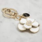 Gold keychain with a white flower charm and a small round tag on a marble surface.