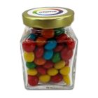 A glass jar filled with colorful candy-coated chocolates and a gold lid.