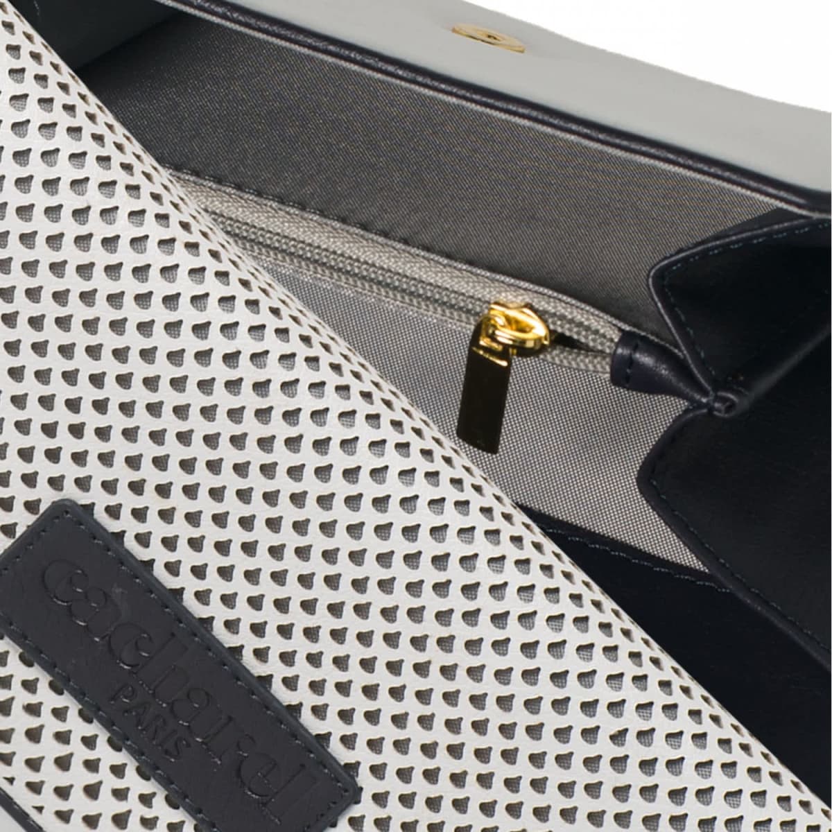Close-up of a white perforated handbag with a gold zipper and black Coachard Paris label.