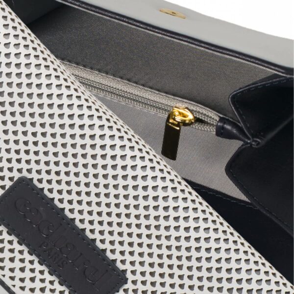 Close-up of a white perforated handbag with a zipper and embossed black label.