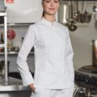 A chef in a white uniform stands confidently in a professional kitchen.