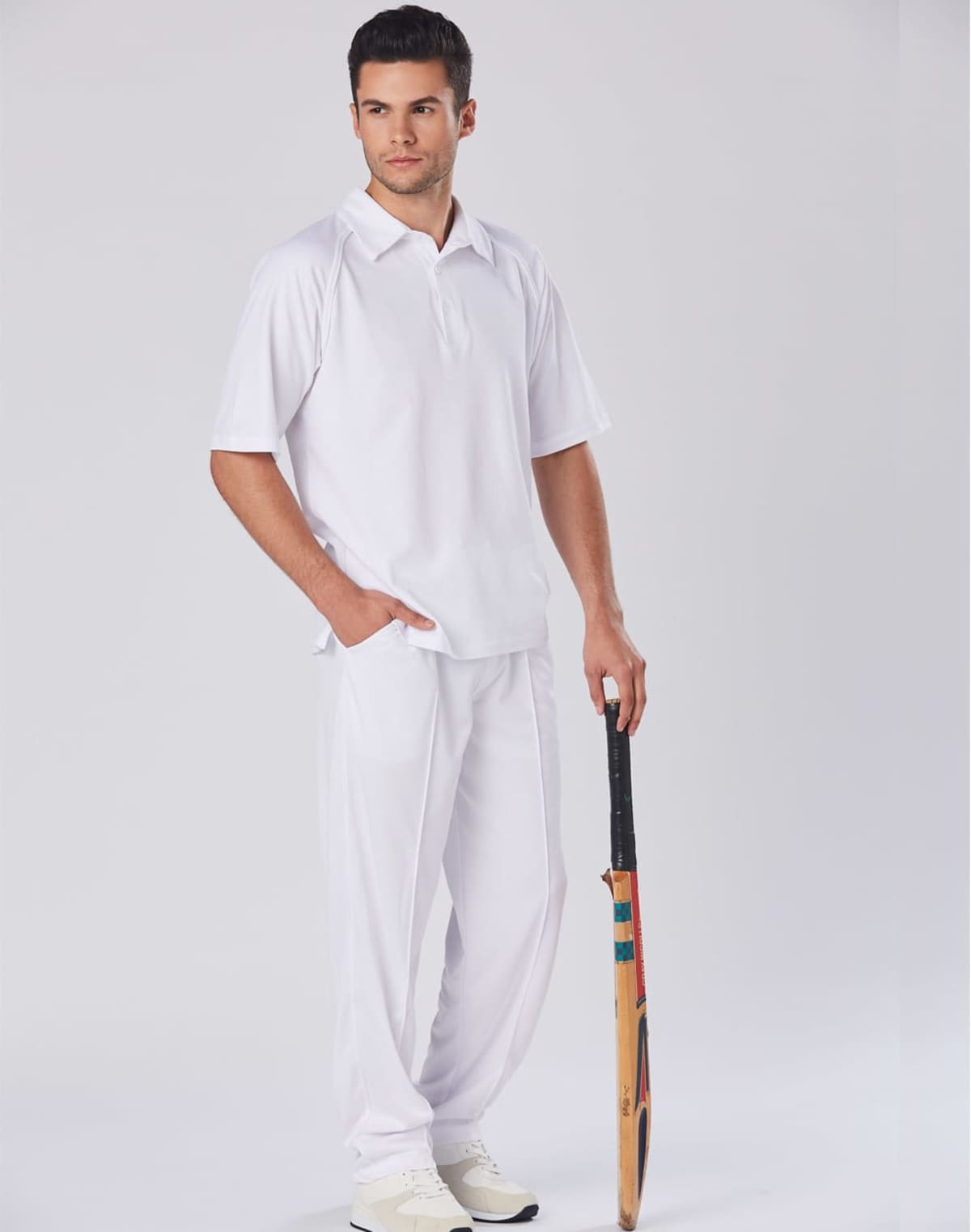 Man in white sportswear holding a cricket bat, standing against a plain background.