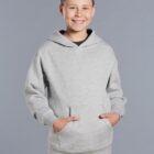 Smiling boy in a light gray hoodie with hands in pockets, standing against a gray background.