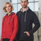 Two people wearing hooded zip-up jackets, one in red and one in black, standing indoors.