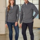 A woman and man wearing gray quarter-zip pullovers and jeans stand indoors.