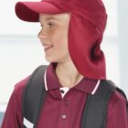 Smiling boy in a maroon sun hat and polo shirt with a backpack, looking to the side.