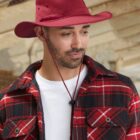 Man in a red hat and plaid shirt with a white undershirt, looking down and smiling.