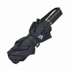 Closed black folding umbrella with a strap around it, lying on a white background.