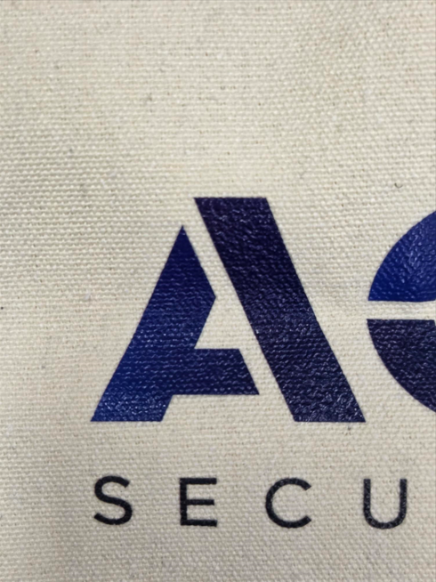 Partial blue A and text SECUR on custom tote bags with a textured beige fabric background.