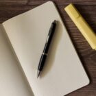 Open dotted notebook with a black pen and a yellow highlighter on a wooden surface.