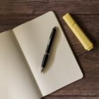 Open dotted notebook with a black pen and yellow highlighter on a wooden table.