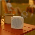 A portable Bluetooth speaker and mug on an orange outdoor table at sunset.
