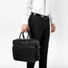 Person in business attire holding a black leather briefcase against a white background.