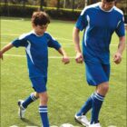 A man and boy in blue uniforms playing soccer on a green field, with SPORTS text below.