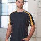 Man wearing a black T-shirt with yellow stripes stands indoors near large windows.