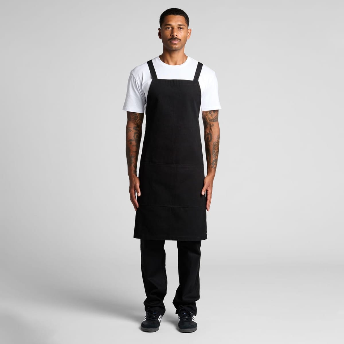 Man standing in a black apron, white shirt, and black pants against a plain background.