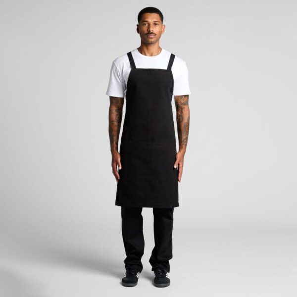 Man wearing a white shirt, black apron, and black pants standing against a plain background.