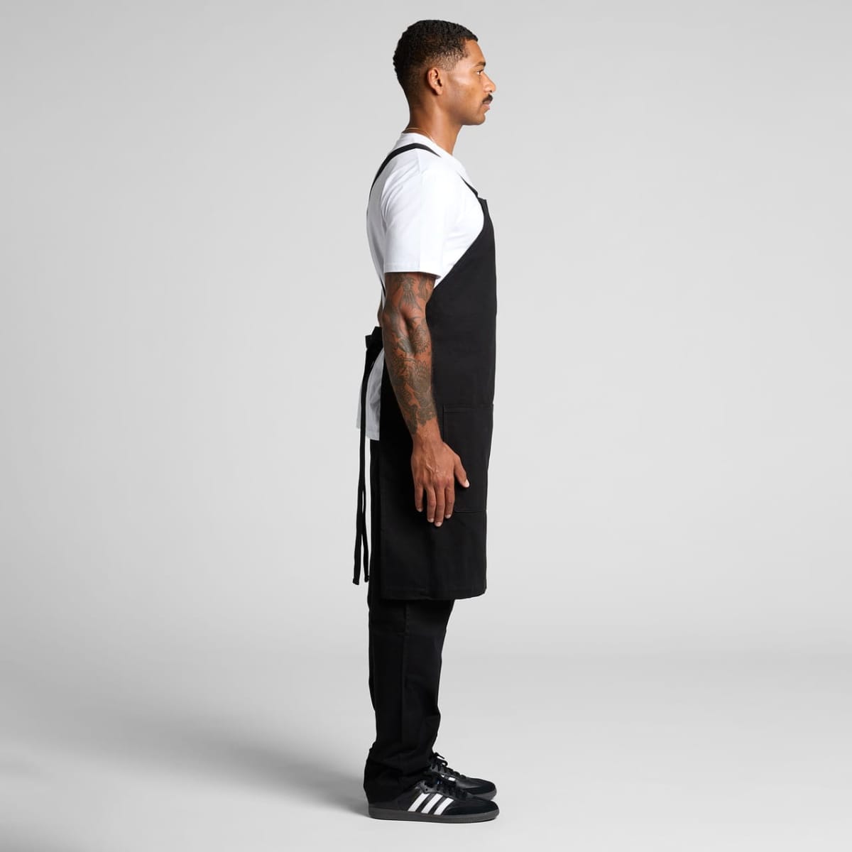 Man in black apron and white t-shirt standing in profile against a plain background.