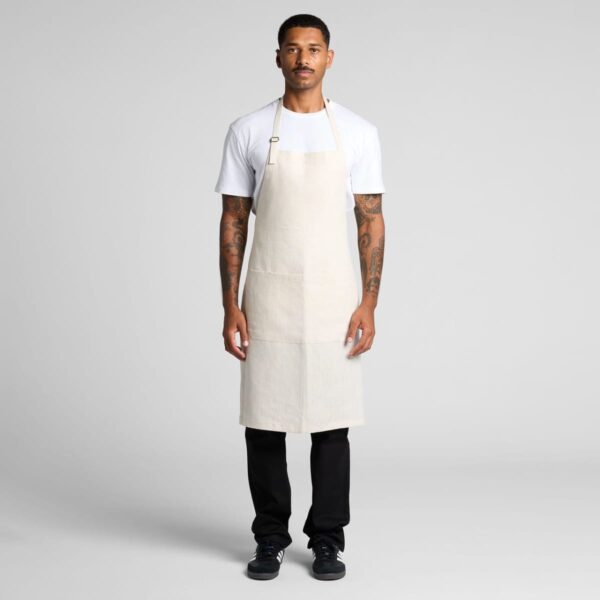 Man in a white t-shirt and beige apron stands facing forward against a plain background.