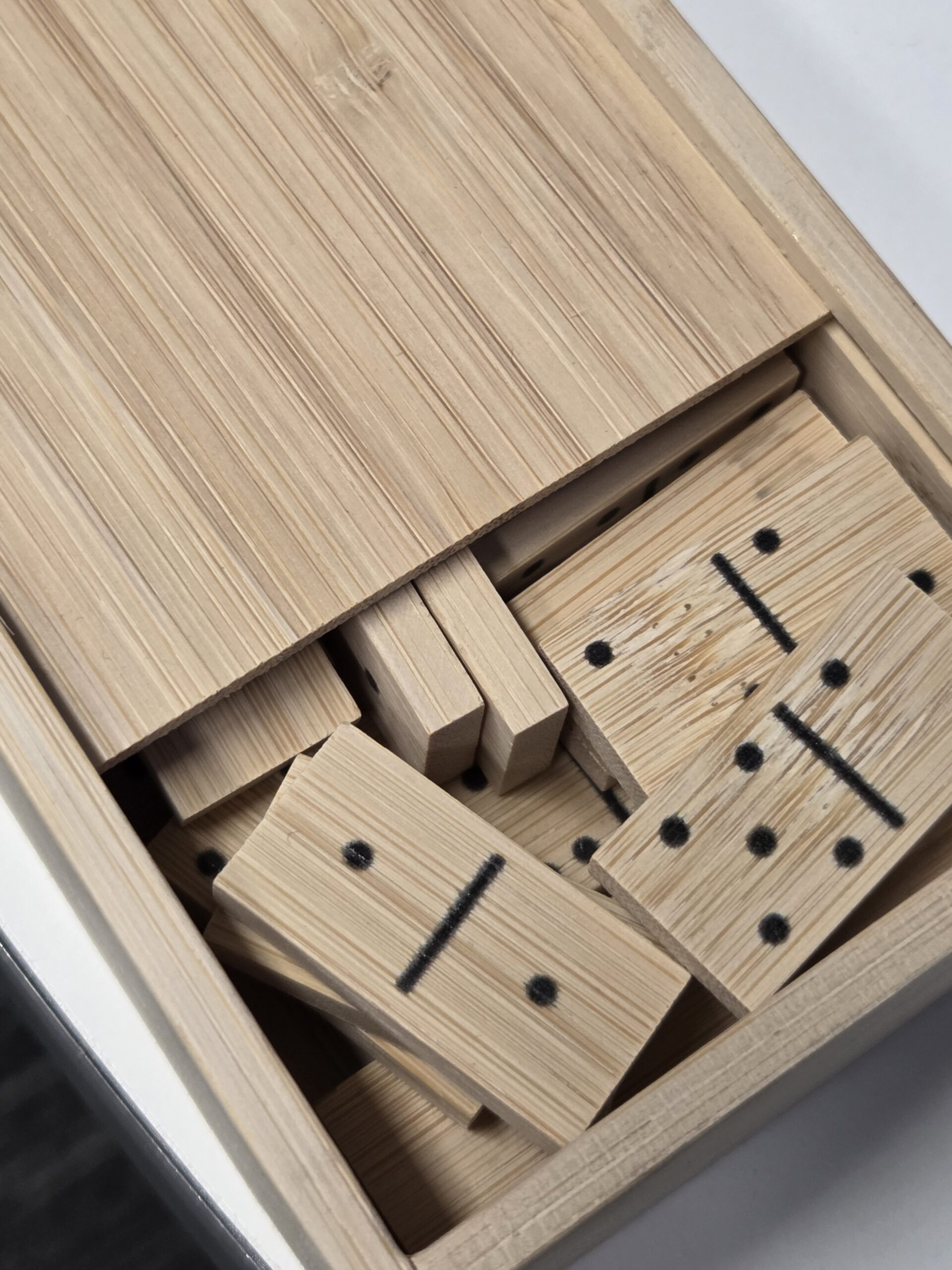 A bamboo wooden box filled with scattered domino tiles, some dots and lines visible.