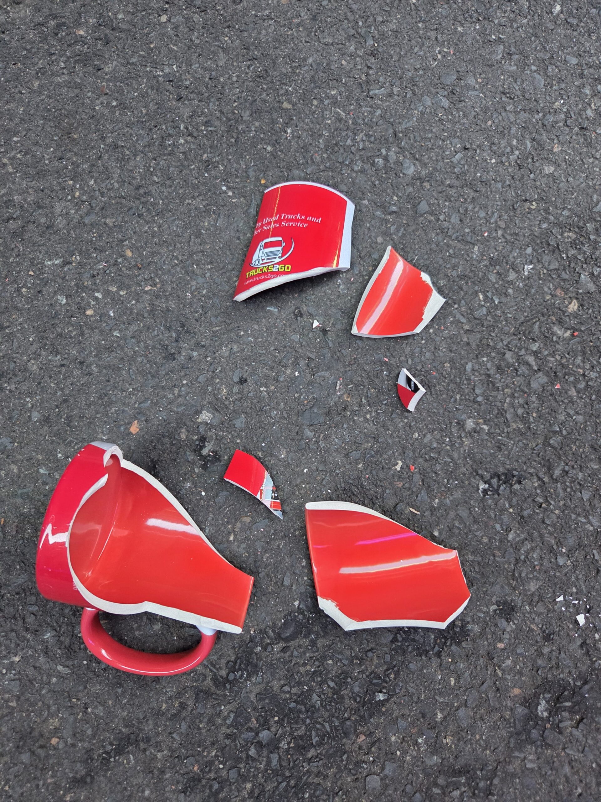 A red ceramic mug, unlike durable porcelain mugs, shattered on a rough gray surface.