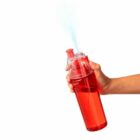 A hand sprays mist from a red water bottle against a white background.