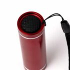 A red cylindrical flashlight with a black textured button and a wrist strap.