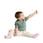 A toddler sitting and reaching upward while holding a small object in their hand.