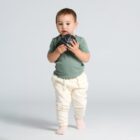 Toddler in green shirt holding a small black ball, standing on a plain background.