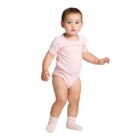 A toddler in a pink onesie and socks standing against a white background.