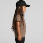 Child in brown t-shirt and black cap standing in profile against a plain gray background.