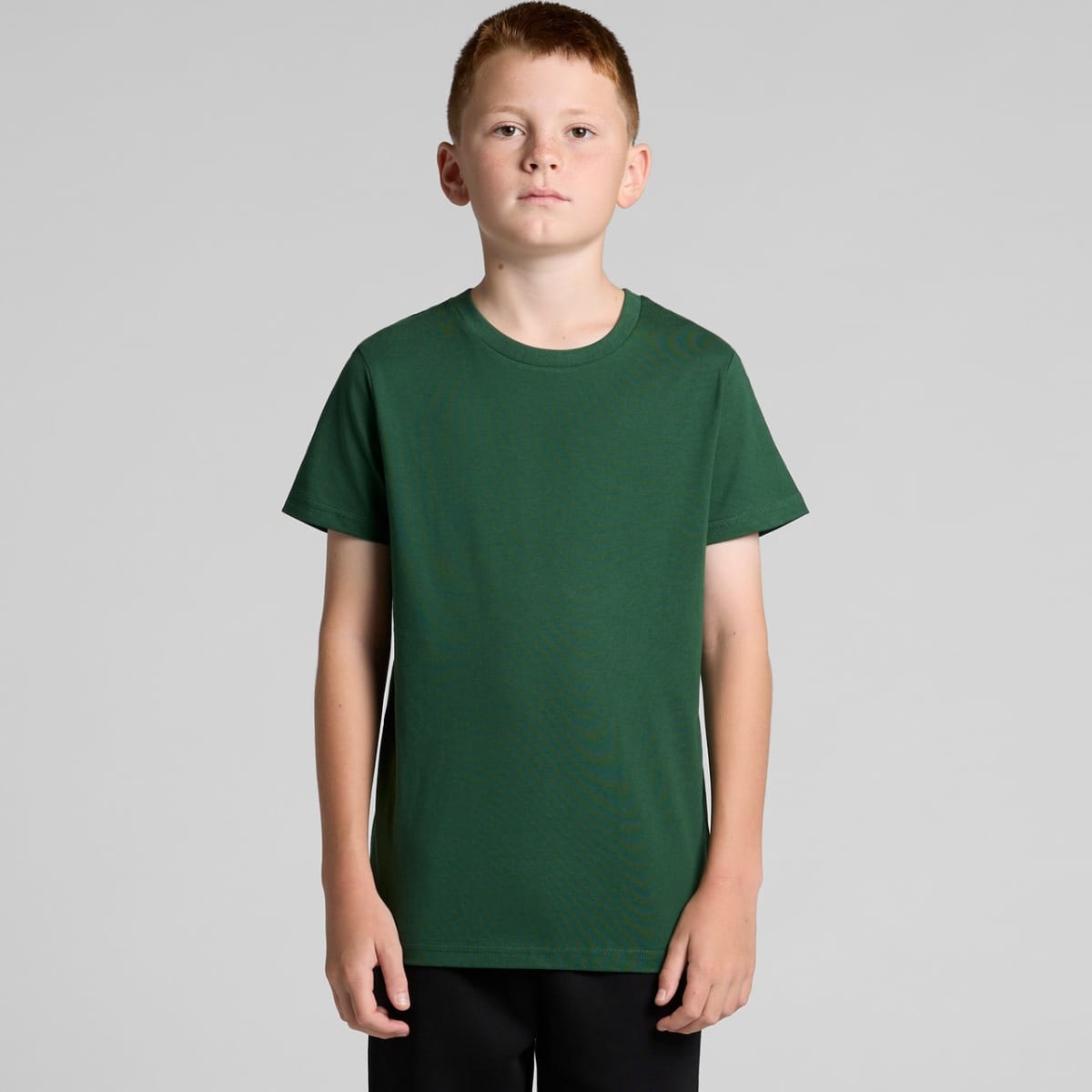 A boy in a green t-shirt and black pants stands against a plain gray background.