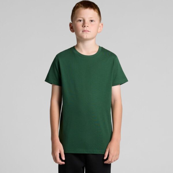 Boy in a plain green t-shirt and black pants standing against a gray background.