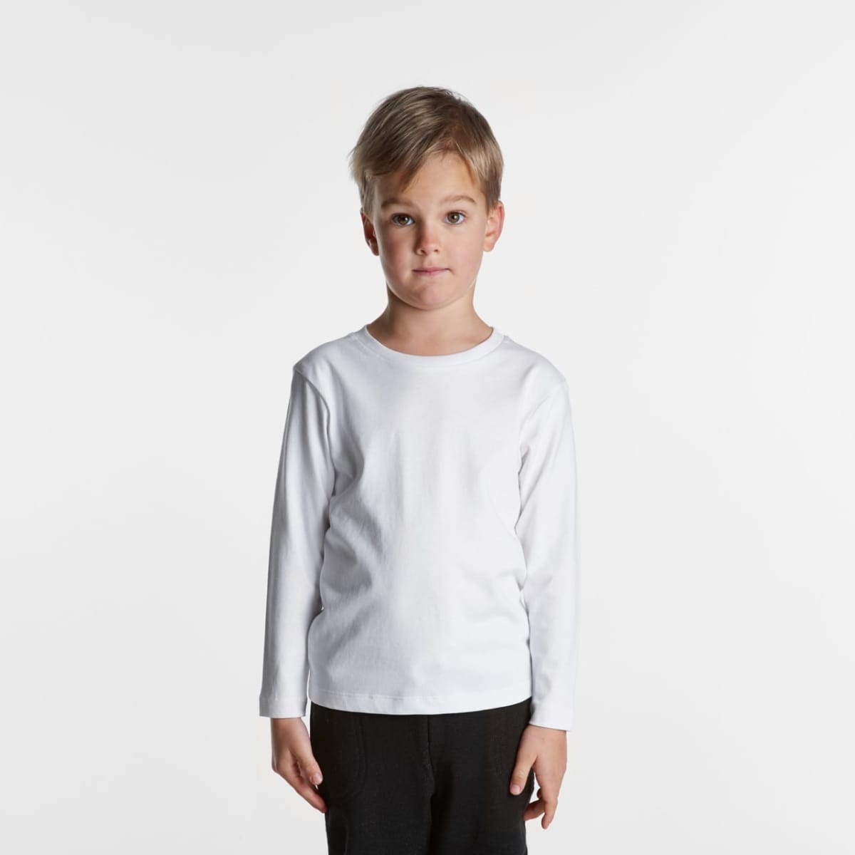 Young boy in a white long-sleeve shirt and black pants standing against a white background.