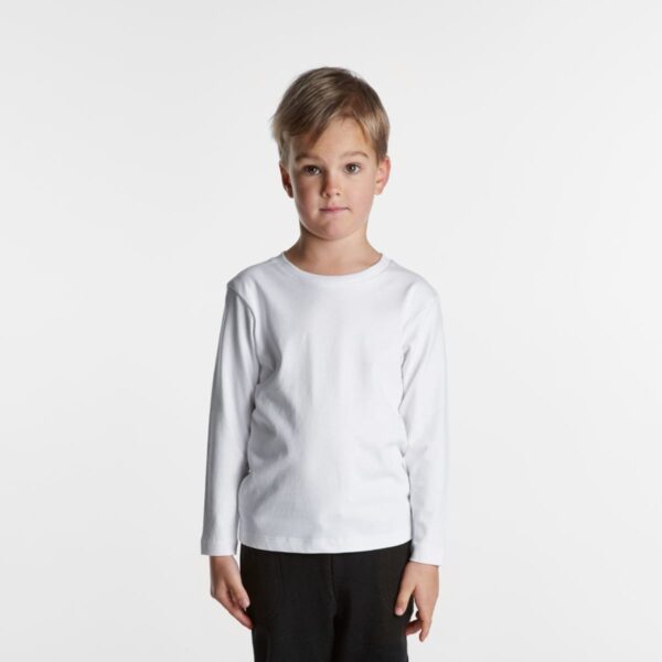 Young boy wearing a plain white long-sleeve shirt and black pants against a white background.