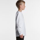 Boy in a white long-sleeve shirt and black pants standing in profile against a white background.